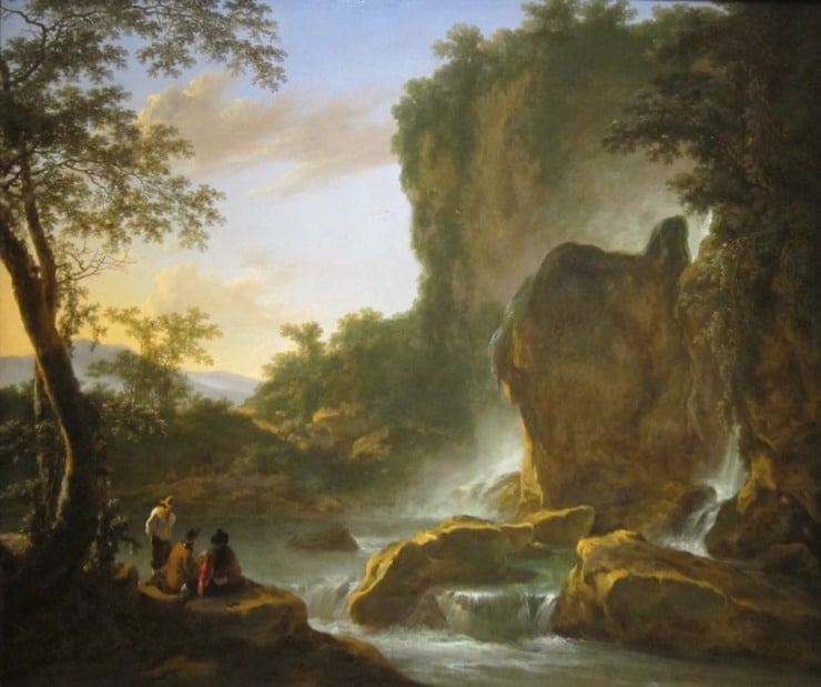 men and women sit outside near a big rock and water, enjoying nature 