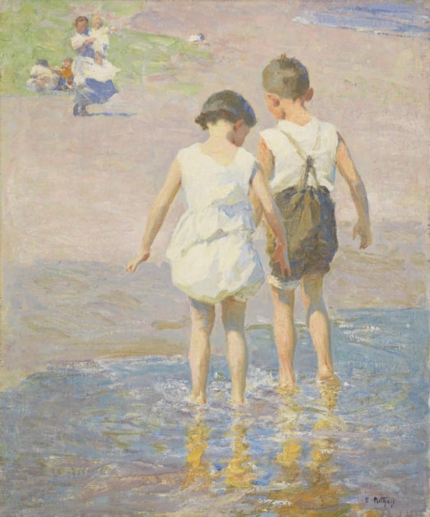 brother and sister walk in the water near a beach 
