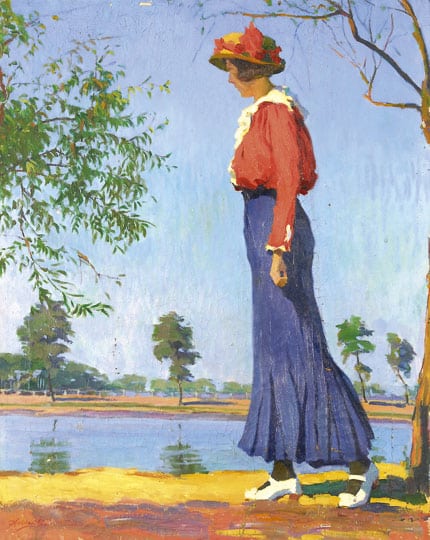 woman walks by a pond wearing a red jacket and blue skirt with a red hat 