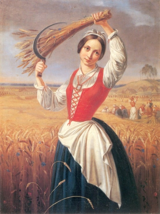 woman stands in field with sickle and stack of wheat 