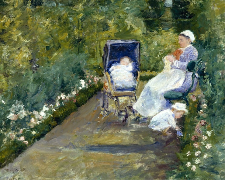 a nannie sits in the garden while a child picks flowers and another one is in a stroller