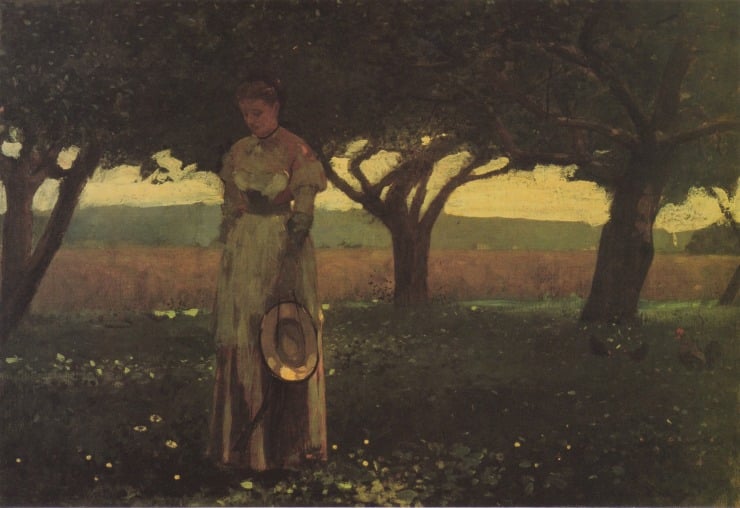 girl holds her hat underneath an orchard 